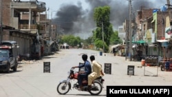 Men watch as smoke rises following an explosion after militants attacked an army base in Pakistan's northwestern city of Bannu on July 15.