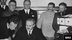 Soviet Foreign Minister Vyacheslav Molotov signs the German–Soviet non-aggression pact. Behind him are Ribbentrop and Stalin.