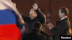 Vladimir Putin (left) greets supporters as President Dmitry Medvedev stands nearby and applauds during a rally in Manezh Square near the Kremlin on March 4, at which Putin declared victory.