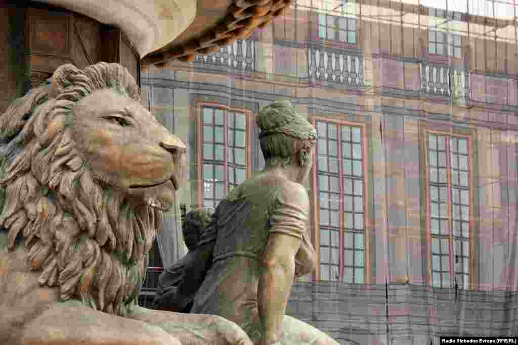 A bronze fountain on a central square honors Olympia, the mother of Alexander the Great. Behind the fountain, a new building facade is under construction.