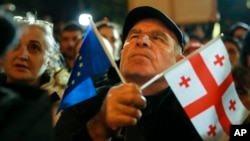 A demonstrator holds an EU and a Georgian national flag at an opposition protest against the results of the parliamentary election in Tbilisi on October 28.