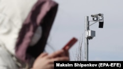 A woman walks past a CCTV camera while checking her phone in Moscow.