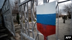 Members of the new pro-Russian forces dubbed the "military forces of the autonomous republic of Crimea" stand at a gate, adorned with a Russian flag, of Simferopol's republican military enlistment complex on March 10.