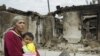 An ethnic Uzbek woman on June 16 carries her child past homes destroyed during the clashes in her village, Kyr-Aryk in the Osh region.