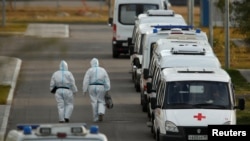 Medical specialists wearing protective gear walk past ambulances outside a hospital for patients infected with the coronavirus on the outskirts of Moscow.